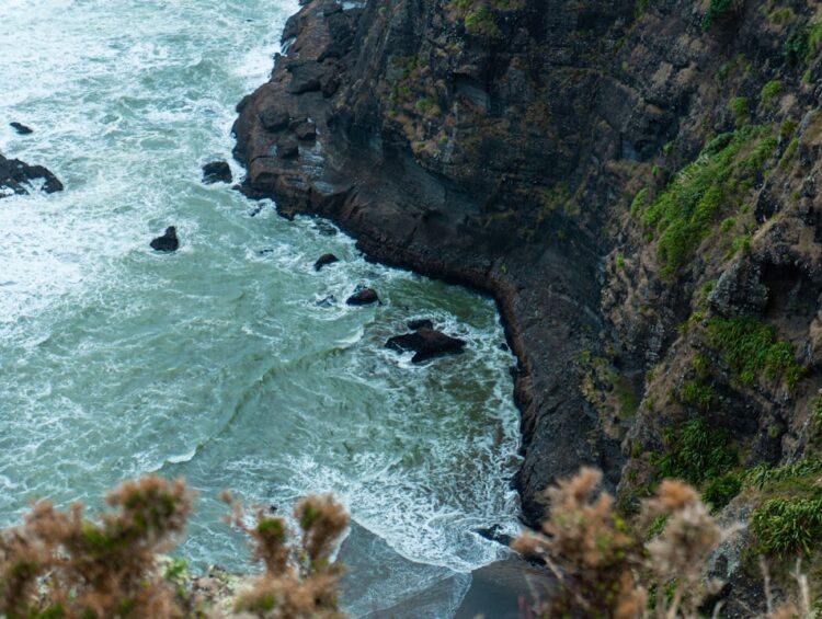 Waves crash against a rocky cliffside with vegetation.