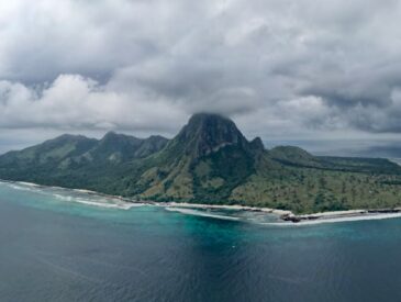 Lush green island with a prominent peak under cloudy sky.