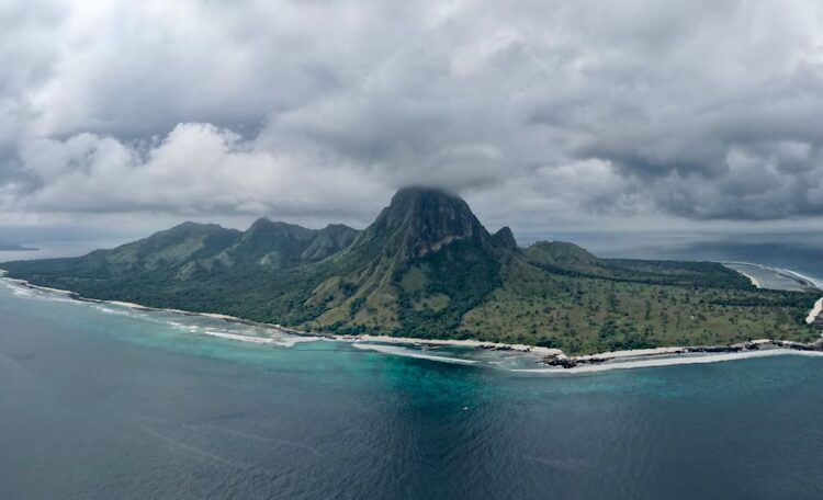 Lush green island with a prominent peak under cloudy sky.
