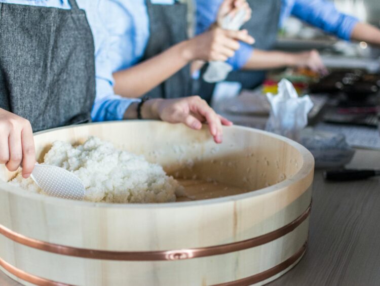 Close-up of sushi rice being prepared by chefs in a bright modern kitchen setting.