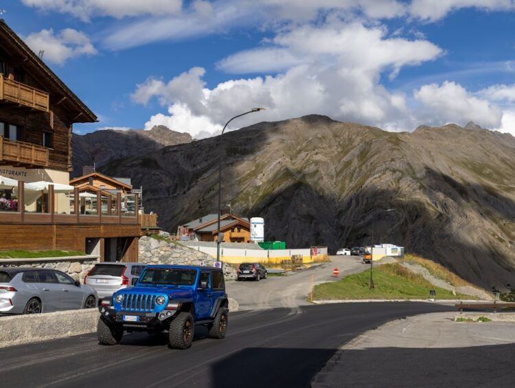 Blue jeep drives on mountain road near buildings.