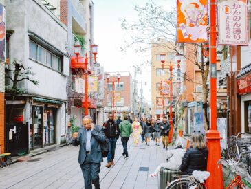 People walking down a narrow street with shops and signs.